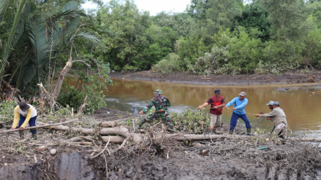 Penuh Lumpur, Anggota Satgas TMMD Bersama Warga Angkut Kayu untuk Jembatan Darurat